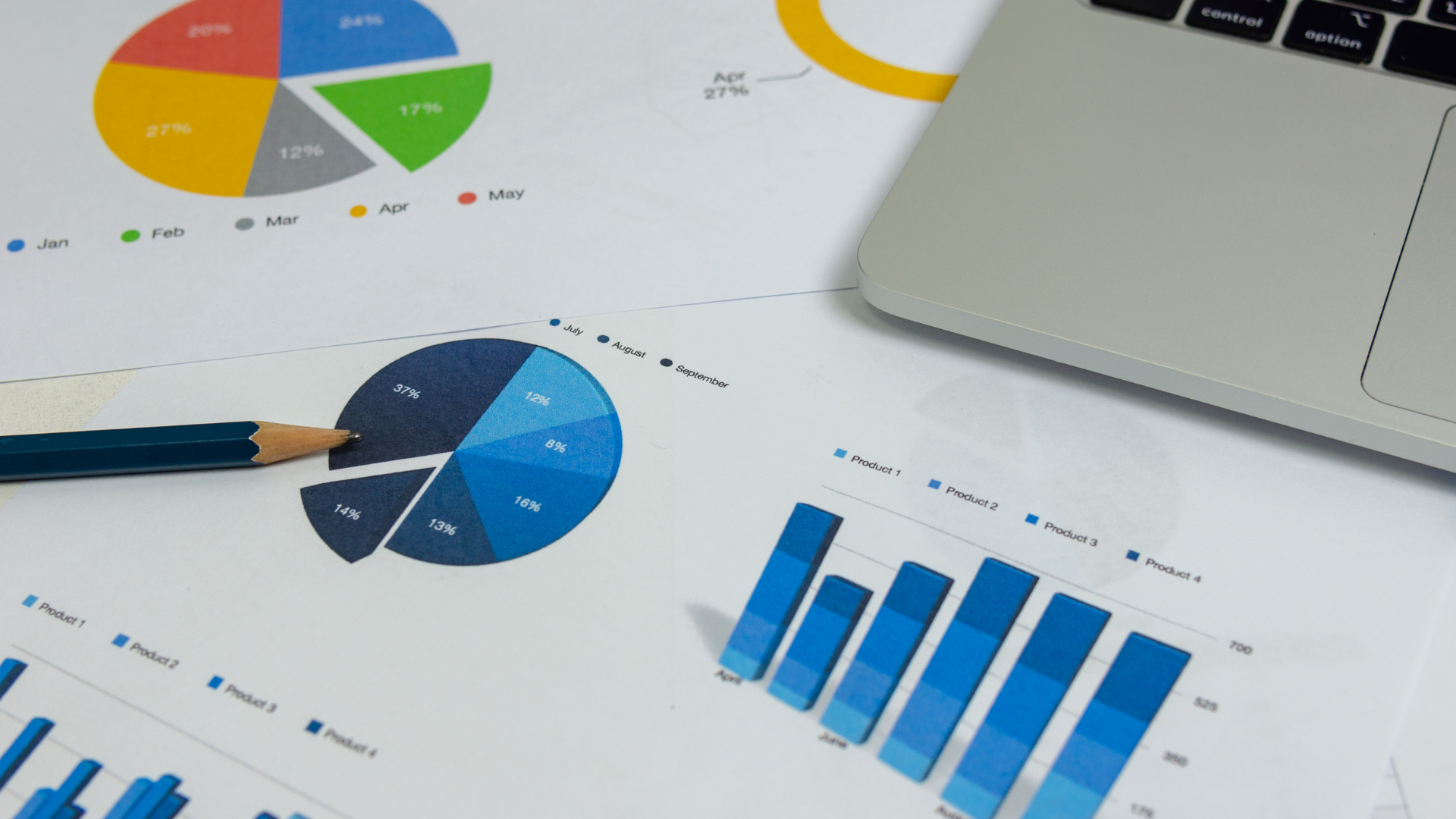 Tableaux de reporting avec graphiques (camemberts et barres) posés près d’un ordinateur portable, illustrant le suivi de performance client.
